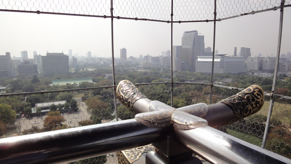 the treed grounds with osaka in the background.  ornate posts meet at the corner in the foreground